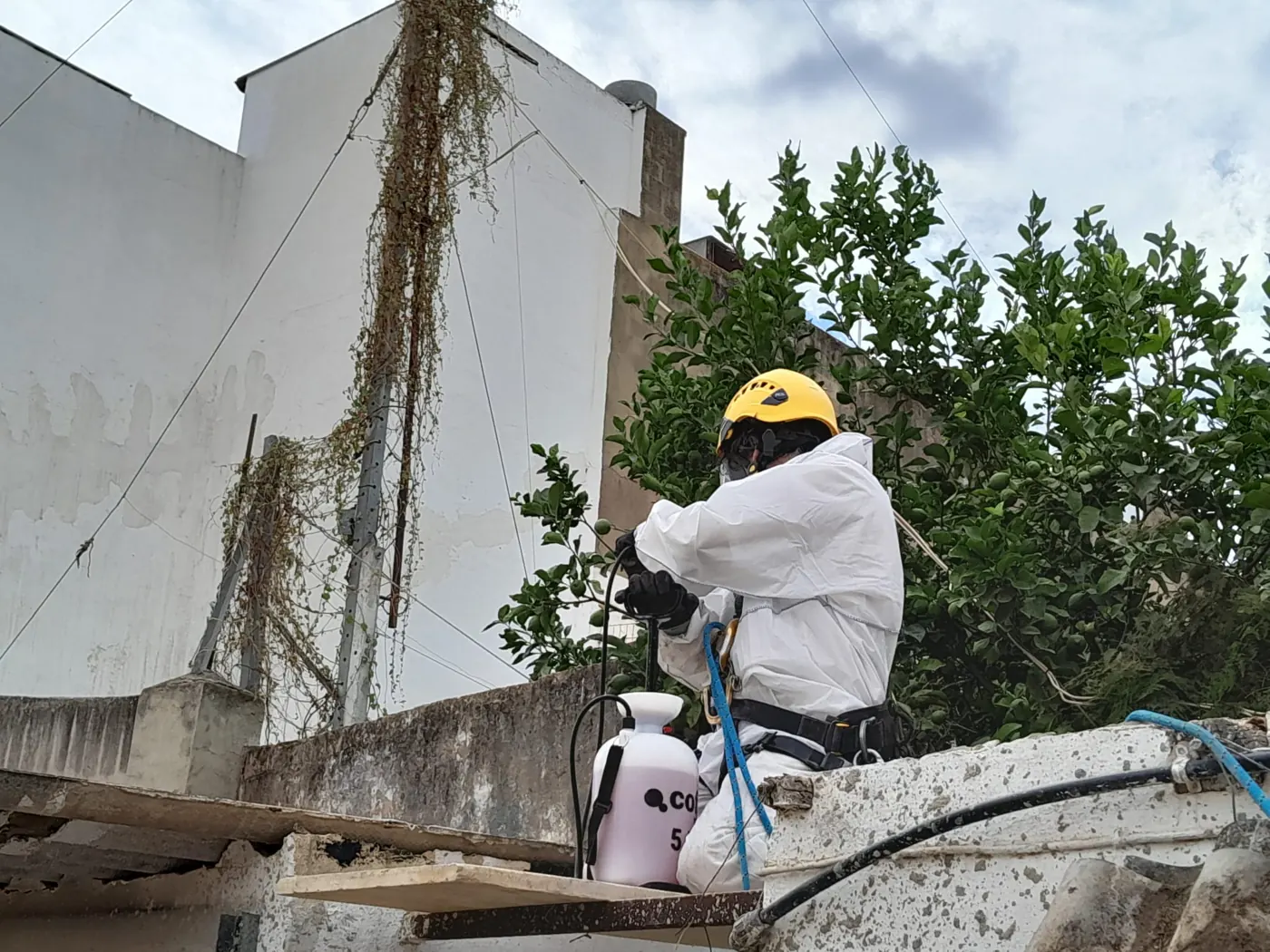Operario con casco y buzo pulverizando agua sobre las placas de fibrocemento en la cubierta