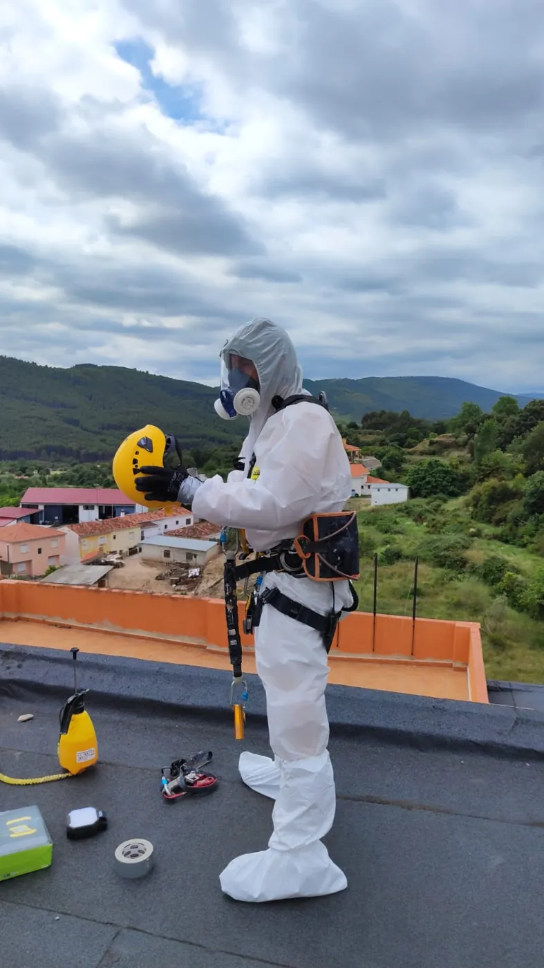 Operario colocándose el casco con buzo desechable, mascarilla y arnés antes de retirar el amianto